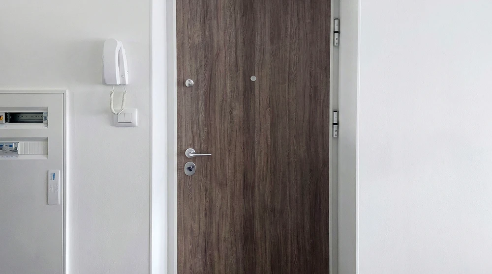 Entrée d'appartement avec porte blindée en stratifié imitation bois foncé, équipée d'une serrure à cylindre européen, d'une béquille en acier inoxydable et d'un verrou de sécurité