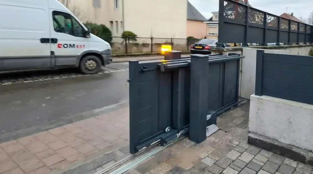 Portail coulissant motorisé en aluminium anthracite, en cours d'ouverture sur une allée en pavés