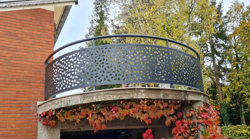 Clôture aluminium gris anthracite avec bande décorative rouge ajourée à motifs végétaux abstraits, devant pavillon de plain-pied blanc aux encadrements rouges assortis