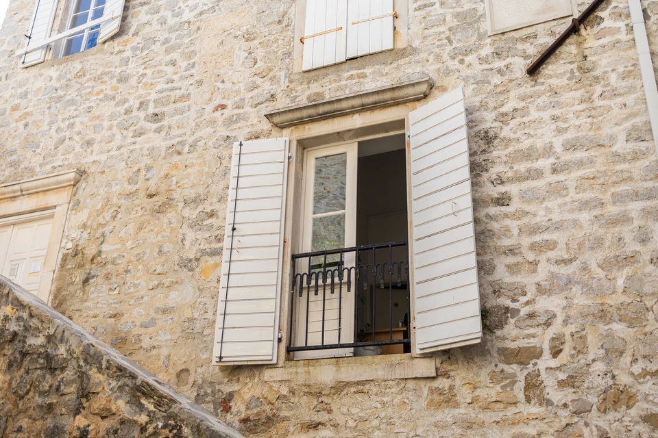 Façade extérieure de bâtiment avec fenêtre équipée d'un volet roulant blanc fermé, encadrée de deux volets battants en bois massif de teinte brune