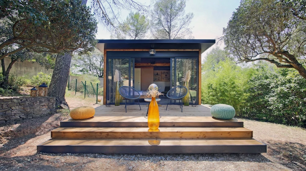 Terrasse en bois composite avec escaliers, devant un studio moderne à ossature bois avec façade vitrée coulissante et toiture monopente